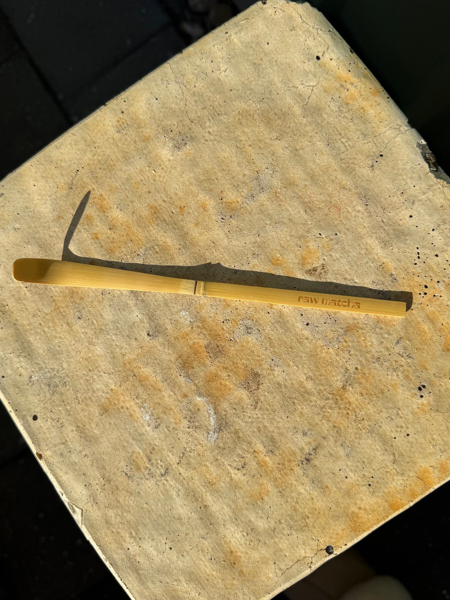 A small curved metal tool with a yellow handle lies on a worn beige stone or concrete surface.